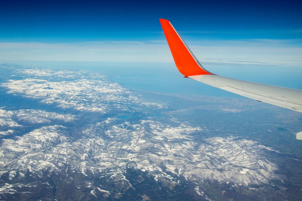 Scenic aerial view of snow-capped mountains from a plane, featuring a vibrant red wing.