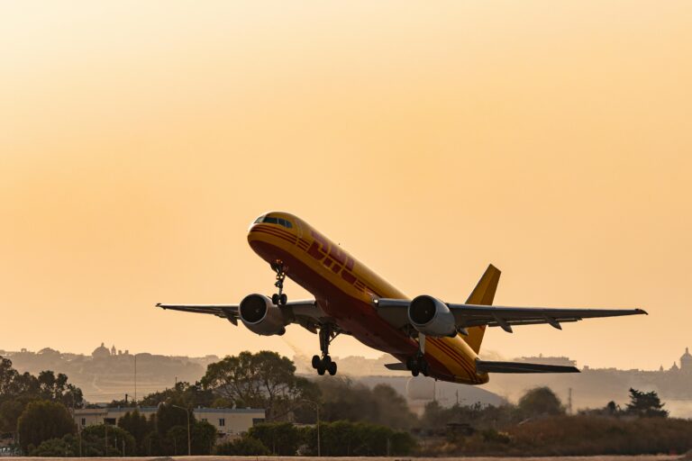A DHL cargo plane takes off against a golden sunset sky, showcasing aviation in action.