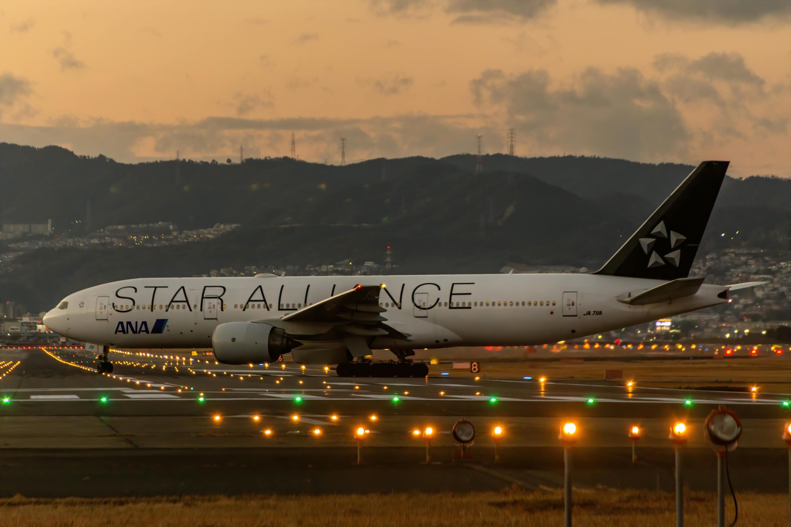Star Alliance Boeing 777 landing at Osaka airport at dusk, capturing the vibrant runway lights and scenic backdrop.